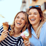 Two young women laughing and holding ice cream in hand